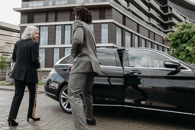 A chauffeur driver in a crisp uniform, providing a corporate limousine services opening the black car door for the client